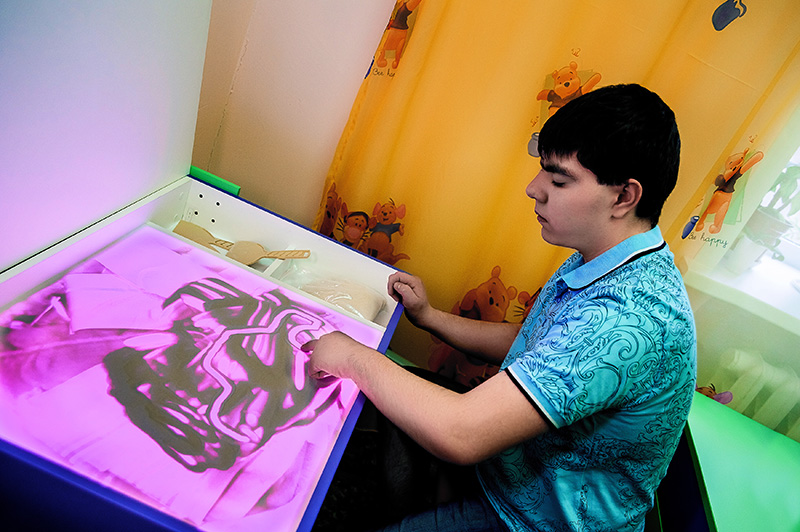 ребенок с ОВЗ работает с Творческой мастерской, рисуя песком