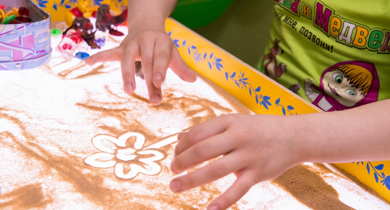 ребенок рисует цветочек с помощью песка на световом столе