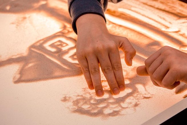 ребенок рисует домик песком